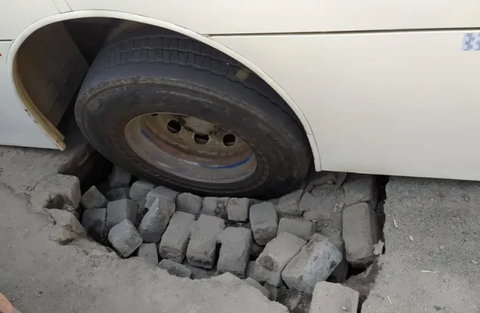 Ônibus fica com roda presa em buraco após parte do asfalto ceder